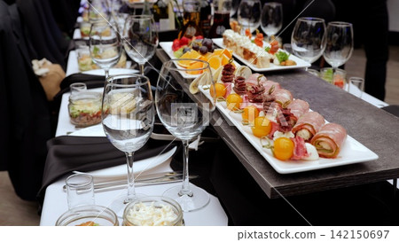 Sophisticating wine glasses surrounding gourmet appetizers, nestled on sleek black tablecloth, highlighting refined culinary styling for upscale catered gathering Sophisticating wine glasses surrounding gourmet appetizers, nestled on sleek black tablecloth, highlighting refined culinary styling for upscale catered gathering 142150697