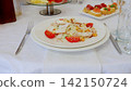 Caesar salad featuring crisp lettuce, grilled chicken, ripe tomatoes, crunchy croutons, and grated parmesan cheese, elegantly plated with silverware on pristine white linen 142150724