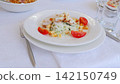Caesar salad presenting grilled chicken, ripe tomatoes, golden croutons, and shaved parmesan cheese, nestled on pristine white ceramic plate with vibrant green lettuce 142150749
