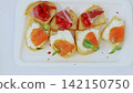Miniature sandwiches featuring assorted gourmet toppings neatly lined up on crisp white plate, presenting elegant appetizer selection for sophisticated dining 142150750