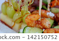 Gourmet catering appetizers featuring grilled shrimp, crisp cucumber, and sweet green grapes arranged with elegant precision on pristine white surface 142150752