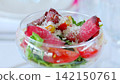 Festive glass dish displaying colorful salad, vibrant tomatoes, crisp arugula, thin dried meat slices, sprinkled parmesan cheese 142150761