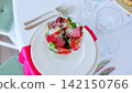 Roasted beef slices layered with ripe tomatoes, peppery arugula, and shredded cheese, served in transparent glass bowl against pristine backdrop 142150766