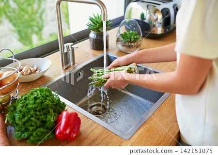 Cooking, kitchen and woman washing vegetables for meal prep, fresh and healthy food for lunch. Diet, wellness and girl at home with ingredients, nutrition and cleaning asparagus in water for dinner Cooking, kitchen and woman washing vegetables for meal prep, fresh and healthy food for lunch. Diet, wellness and girl at home with ingredients, nutrition and cleaning asparagus in water for dinner 142151075