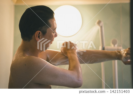 A man washing his arms in the shower during his bath time. A man washing his arms in the shower during his bath time. 142151403