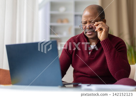 Mature black man straining eyes while adjusting glasses at laptop Mature black man straining eyes while adjusting glasses at laptop 142152123
