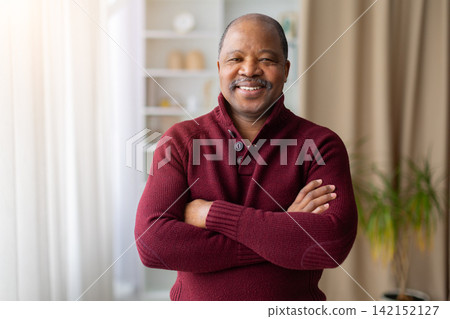 Confident mature Black man standing at home with arms crossed Confident mature Black man standing at home with arms crossed 142152127