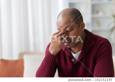 Mature Black man pinching the bridge of his nose, showing headache Mature Black man pinching the bridge of his nose, showing headache 142152145