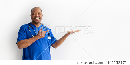 Smiling Black doctor in blue scrubs presenting copy space with open hand Smiling Black doctor in blue scrubs presenting copy space with open hand 142152171