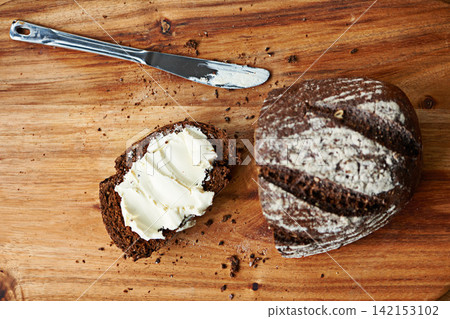 Sourdough, bread and butter on slice for meal, nutrition and carbs on kitchen table or fibre. Top view, wheat and rye snack on cutting board, grain and organic ingredients for artisan food in home 142153102
