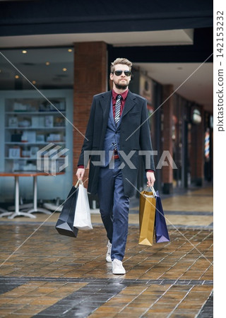 Man, shopping bags and formal clothes at mall, walking and customer or shopper, discount and retail. Boutique, sale and spree in sunglasses, suit and purchase in product, deal and stylist in city 142153232