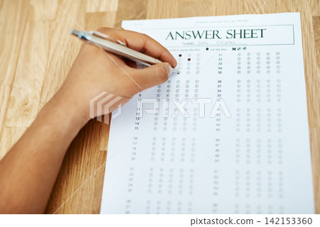 Hand of person, test and answer sheet on table for exam, education and student writing quiz in college. Assessment, document and pen to tick circle, paper and multiple choice with questions on desk 142153360