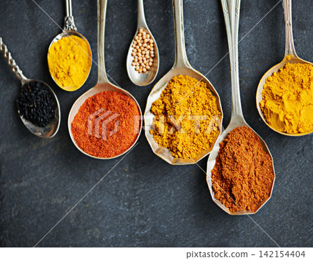 Above, spices and spoon for flavor and dry ingredient for cooking, cuisine and food on table top for traditional Indian dish. Paprika, cayenne and curry powder with masala and cumin for hot dinner Above, spices and spoon for flavor and dry ingredient for cooking, cuisine and food on table top for traditional Indian dish. Paprika, cayenne and curry powder with masala and cumin for hot dinner 142154404