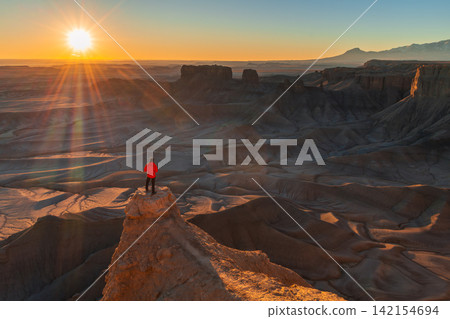 Peaceful solitary hiker standing on high rock cliff watching golden sunrise over vast desert canyon landscape in utah full of wonder Peaceful solitary hiker standing on high rock cliff watching golden sunrise over vast desert canyon landscape in utah full of wonder 142154694