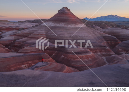 Aerial view shows peaceful hiker exploring colorful striped bentonite hill formation in utah desert landscape during scenic twilight Aerial view shows peaceful hiker exploring colorful striped bentonite hill formation in utah desert landscape during scenic twilight 142154698