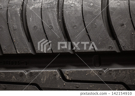 A close-up of a car tire tread, revealing a detailed view of the rubber pattern. Macro photography of the tread of a new car tire, showing a clearly defined pattern. A close-up of a car tire tread, revealing a detailed view of the rubber pattern. Macro photography of the tread of a new car tire, showing a clearly defined pattern. 142154910