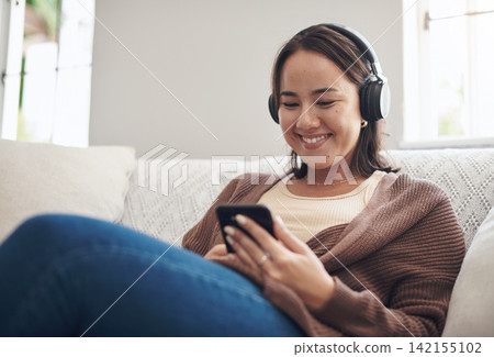 Happy woman, headphones and listening with phone to music on sofa for audio streaming or weekend at home. Female person with smile, relax or enjoying sound track on mobile smartphone in living room 142155102