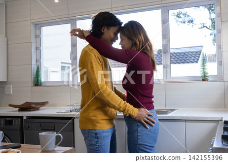Asian couple standing close in home kitchen, touching foreheads near steel sink and mug Asian couple standing close in home kitchen, touching foreheads near steel sink and mug 142155396