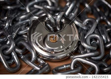 Security, steel and chain with lock for safety on wooden surface for privacy or protection. Metal, equipment and iron padlock and link shackles on table for password or guard with key for secret. Security, steel and chain with lock for safety on wooden surface for privacy or protection. Metal, equipment and iron padlock and link shackles on table for password or guard with key for secret. 142155415