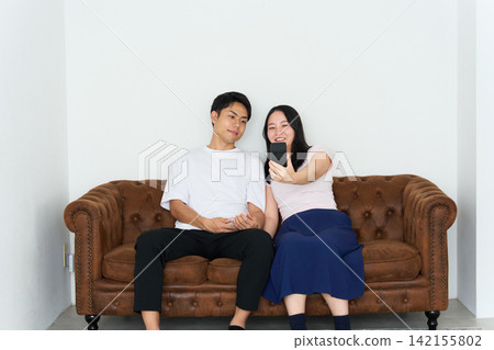 A young man and woman looking at their smartphones on a sofa A young man and woman looking at their smartphones on a sofa 142155802