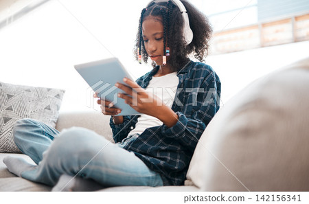 Digital tablet, black girl and headphones on sofa for elearning, education or learning in living room. Technology, person and teenager for streaming videos, play online games or relax in home Digital tablet, black girl and headphones on sofa for elearning, education or learning in living room. Technology, person and teenager for streaming videos, play online games or relax in home 142156341