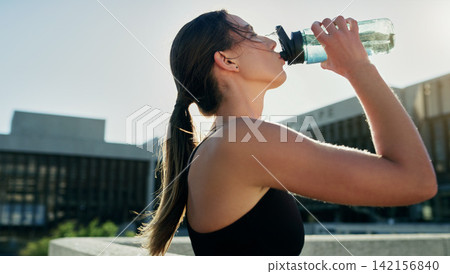 City, profile or woman drinking water on break in exercise, running workout or fitness training. Girl athlete, relax or thirsty sports runner with liquid bottle for wellness or hydration in England City, profile or woman drinking water on break in exercise, running workout or fitness training. Girl athlete, relax or thirsty sports runner with liquid bottle for wellness or hydration in England 142156840