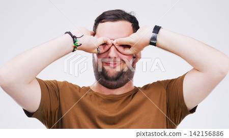 Studio, man and binoculars with hands for crazy comic, silly and goofy expression with smile. Face, male model and goggles sign, symbol and emoji for feedback or reaction by white background Studio, man and binoculars with hands for crazy comic, silly and goofy expression with smile. Face, male model and goggles sign, symbol and emoji for feedback or reaction by white background 142156886