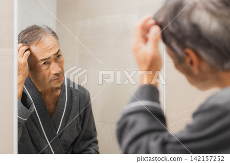 Senior man troubled looking at the mirror Senior man troubled looking at the mirror 142157252