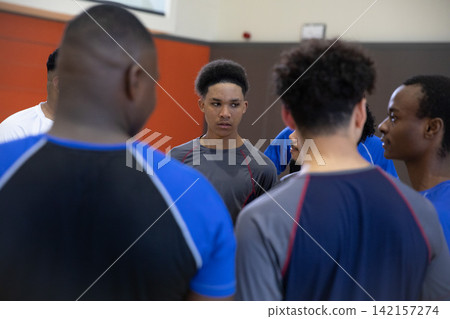 African American teenage males huddling in gymnasium, teen wearing grey athletic top with red seams African American teenage males huddling in gymnasium, teen wearing grey athletic top with red seams 142157274