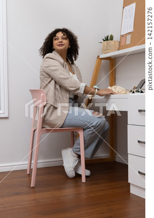 African American woman sitting at white desk in study corner using laptop wearing beige blazer African American woman sitting at white desk in study corner using laptop wearing beige blazer 142157276