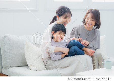 一位家長、一個孩子和他們的祖母坐在沙發上。 一位家長、一個孩子和他們的祖母坐在沙發上。 142158412