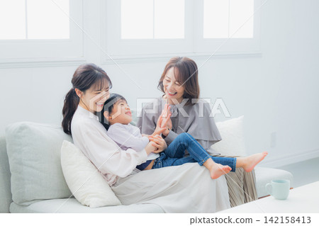 一位家長、一個孩子和他們的祖母坐在沙發上。 142158413