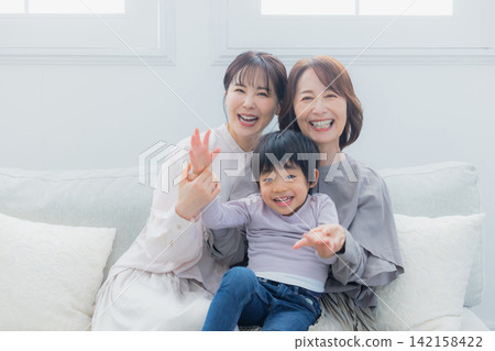 一位家長、一個孩子和他們的祖母坐在沙發上。 一位家長、一個孩子和他們的祖母坐在沙發上。 142158422