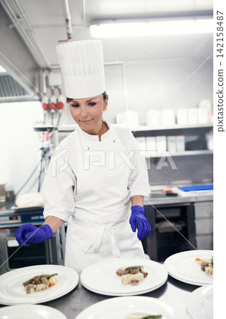 Cooking, chef and woman in restaurant kitchen for catering with food plate for fine dining or hospitality. Expert, culinary professional and worker preparing meal, lunch or dinner for hotel service Cooking, chef and woman in restaurant kitchen for catering with food plate for fine dining or hospitality. Expert, culinary professional and worker preparing meal, lunch or dinner for hotel service 142158487