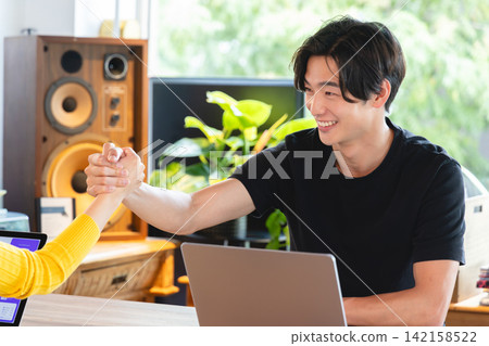 Young business people clasp hands tightly and pledge their cooperation in the office of a venture company. Young business people clasp hands tightly and pledge their cooperation in the office of a venture company. 142158522