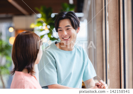 A man and woman in their twenties enjoying a pleasant conversation by the window of a cafe. A man and woman in their twenties enjoying a pleasant conversation by the window of a cafe. 142158541