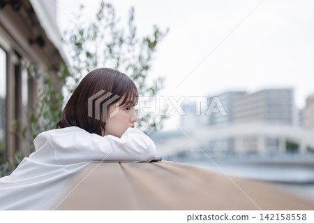 一位女士側臉靠在露台的吧台上,下巴擱在檯面上,沉思著自己的未來和職業道路。 一位女士側臉靠在露台的吧台上,下巴擱在檯面上,沉思著自己的未來和職業道路。 142158558
