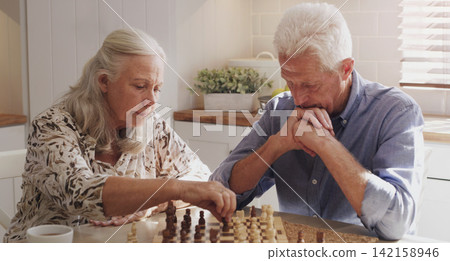 Senior, retired and couple at home with chess on board game by bonding, thinking and strategy for decision. Elderly, man and woman in kitchen with love, relax and trust for challenge of skills Senior, retired and couple at home with chess on board game by bonding, thinking and strategy for decision. Elderly, man and woman in kitchen with love, relax and trust for challenge of skills 142158946
