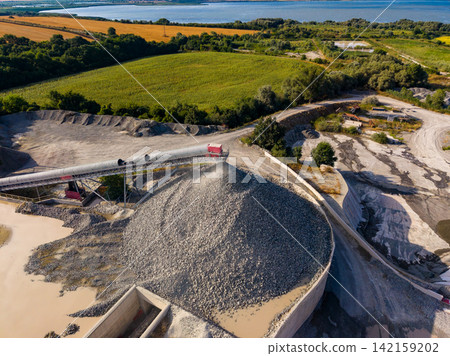 Granite quarry operations with machinery and stone piles near a river and fields on a sunny day Granite quarry operations with machinery and stone piles near a river and fields on a sunny day 142159202