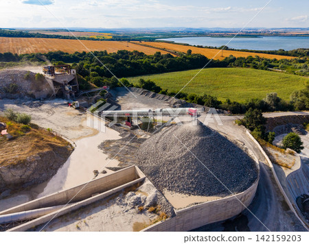 Construction site shows machinery working on gravel pile by the river with fields in the background during the day Construction site shows machinery working on gravel pile by the river with fields in the background during the day 142159203