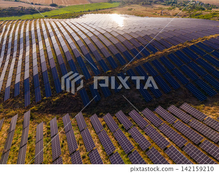 Solar panels cover a large area in a rural setting with farmland and hills in the background during the day Solar panels cover a large area in a rural setting with farmland and hills in the background during the day 142159210