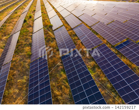 Solar panels cover a large field during the late afternoon sunlight with shadows stretching across the ground Solar panels cover a large field during the late afternoon sunlight with shadows stretching across the ground 142159217