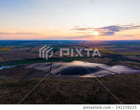 Sunset over solar panels in a field near a rural area with rolling hills and open landscape Sunset over solar panels in a field near a rural area with rolling hills and open landscape 142159225