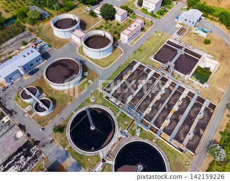 Large wastewater treatment facility with multiple tanks and buildings located in an industrial area on a sunny day Large wastewater treatment facility with multiple tanks and buildings located in an industrial area on a sunny day 142159226