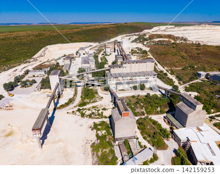 Quarry site with machinery and processing areas in a landscape with hills and clear sky Quarry site with machinery and processing areas in a landscape with hills and clear sky 142159253
