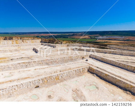 Large quarry shows active site in daytime with vehicles moving across layers of stone and earth Large quarry shows active site in daytime with vehicles moving across layers of stone and earth 142159256