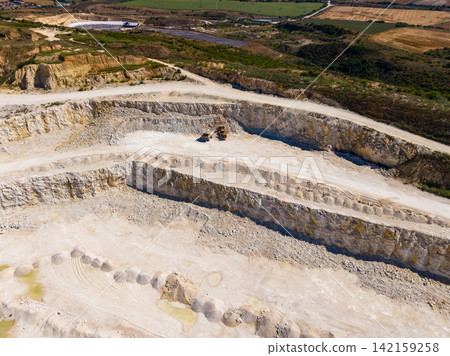 Large quarry with machinery and layered stone formations in an open area from a high viewpoint during daylight hours Large quarry with machinery and layered stone formations in an open area from a high viewpoint during daylight hours 142159258