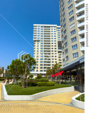 Modern buildings stand next to a green park with trees and benches under a clear blue sky in the daytime Modern buildings stand next to a green park with trees and benches under a clear blue sky in the daytime 142159354