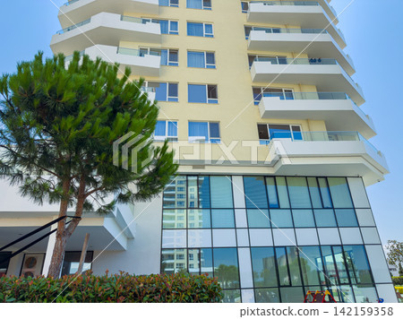 Building with multiple floors and large windows in a sunny location with a tree in the foreground 142159358