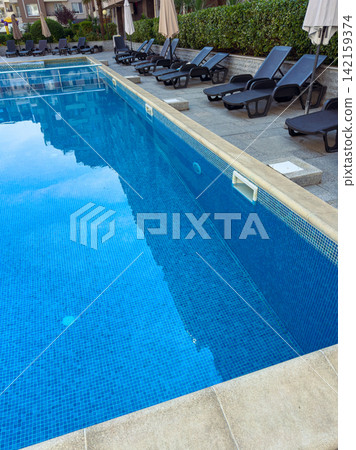 Swimming pool area with lounge chairs and clear water in a hotel setting during the day 142159374